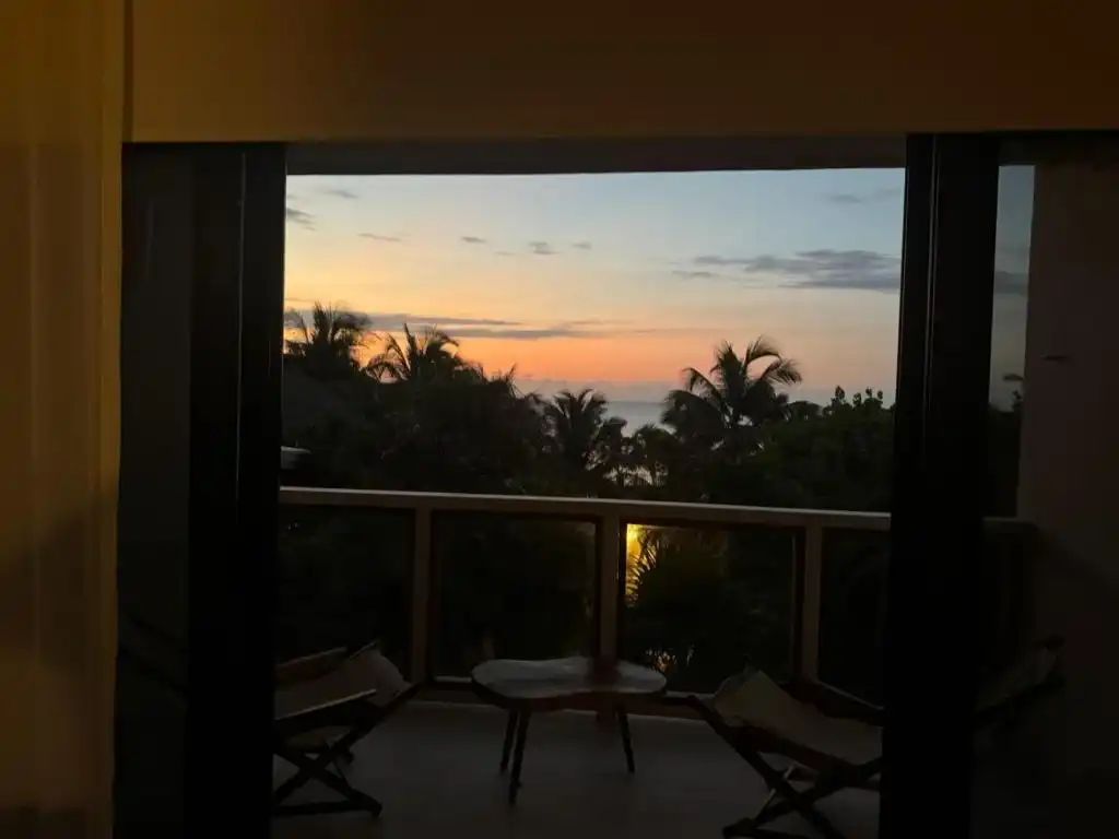 El balcón al atardecer desde dentro del cuarto, con dos sillas.