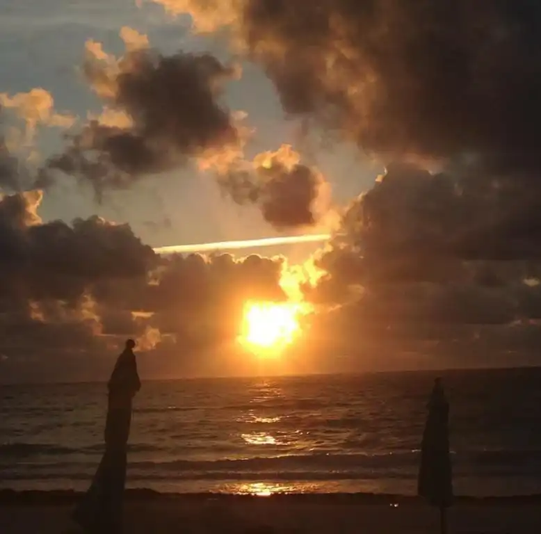 Atardecer nublado sobre el mar, con el sol bajo en el horizonte.