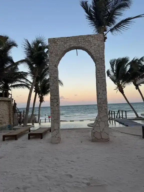 Arco de piedra en la playa entre las palmeras, al atardecer.