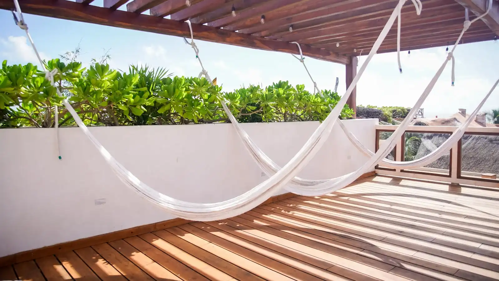 Hamacas blancas colgadas bajo la pérgola de la azotea, sobre el entarimado de madera.