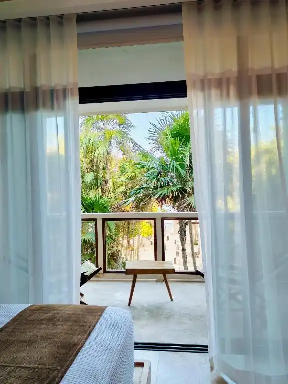 Cama junto al ventanal, con las cortinas abiertas al balcón.
