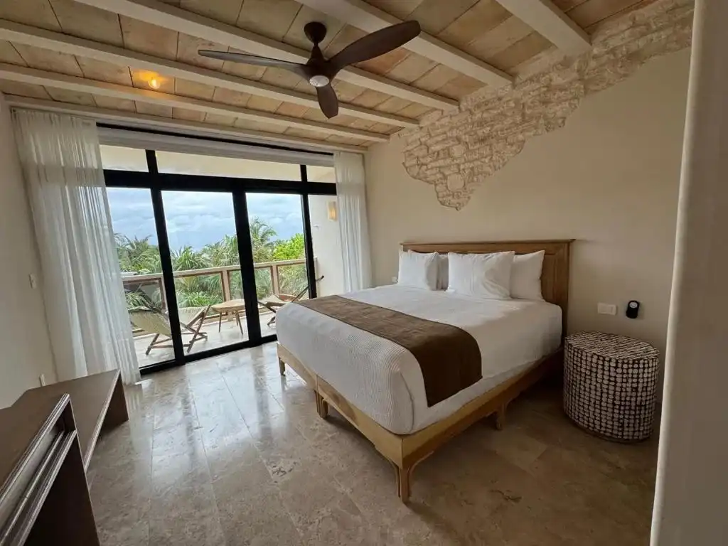Habitación con cama, ventilador de techo y ventanal al balcón.