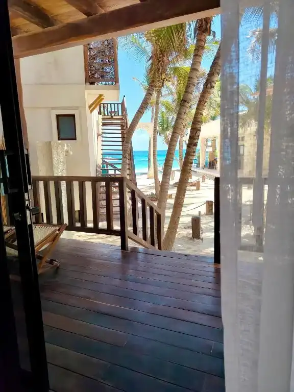 Terraza de madera con palmeras y el mar al fondo.