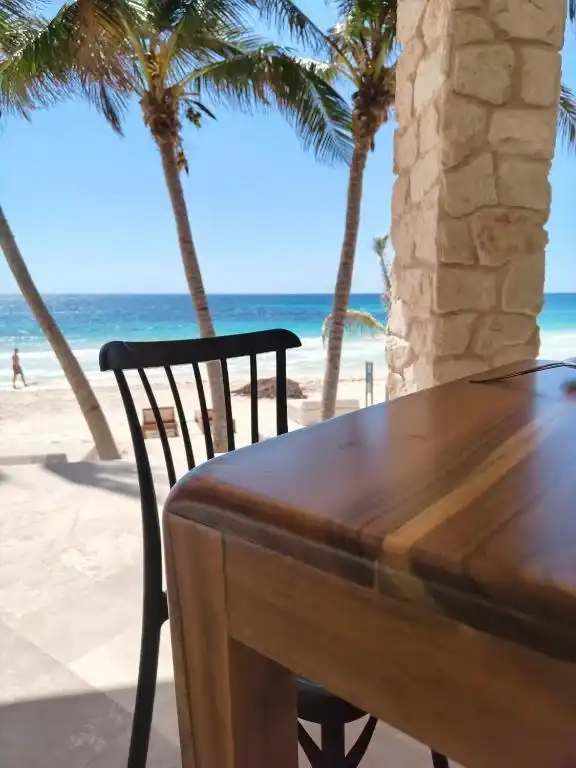 Mesa de madera en la terraza, con las palmeras y el mar detrás.