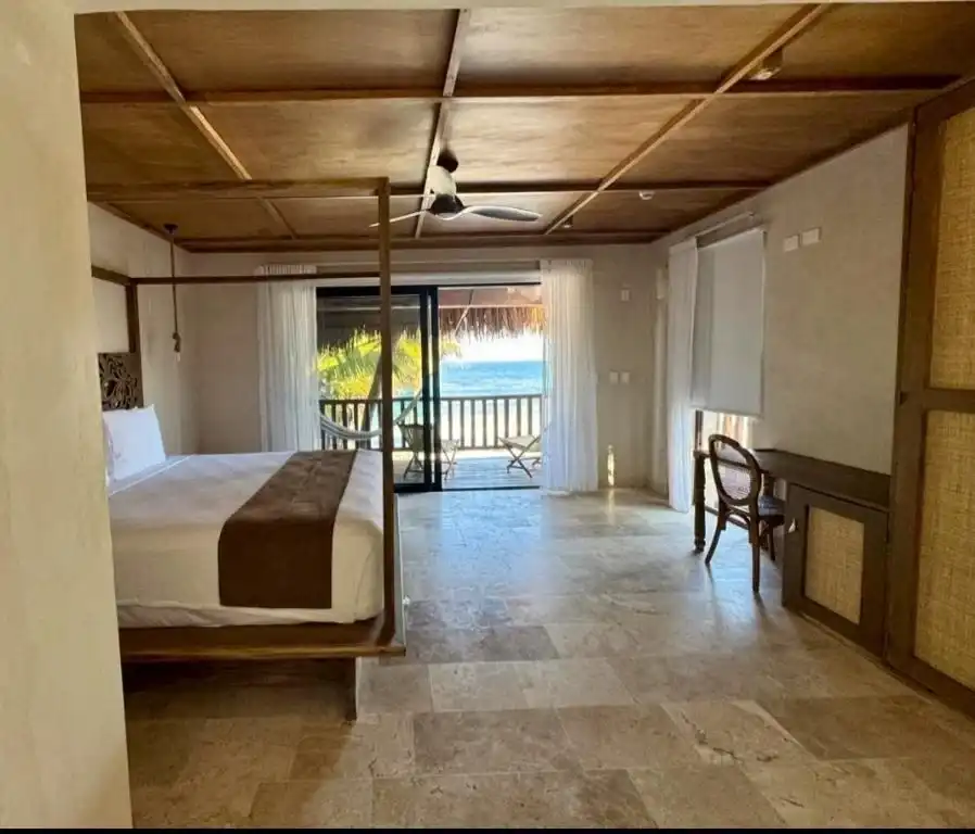 Habitación con techo de madera y salida al balcón, con el mar al fondo.