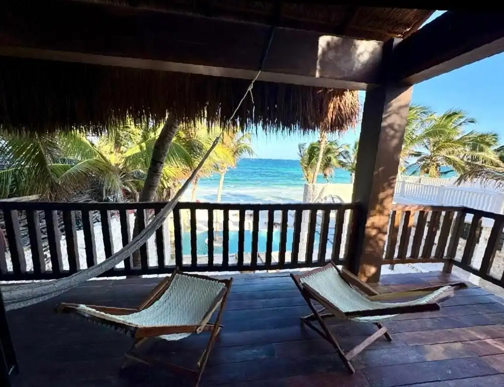 Terraza bajo palapa con dos sillas de tijera, frente al mar.