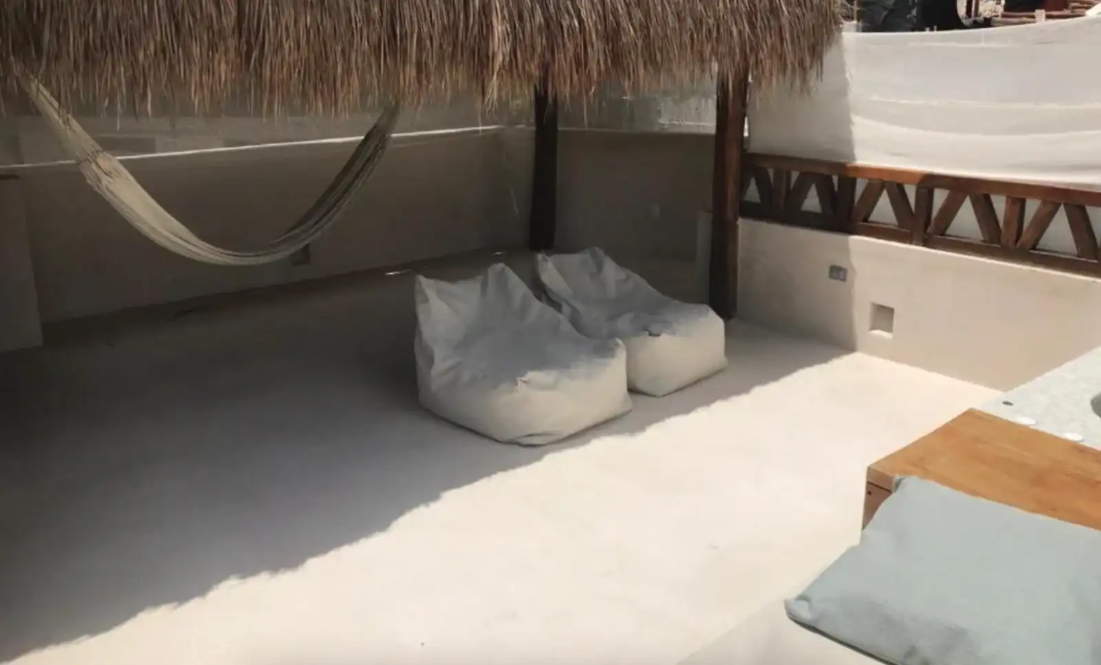 Rincón bajo techo de palma con una hamaca, dos pufs y una mesa baja de madera.