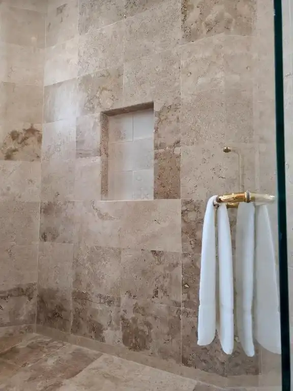 Regadera con las toallas colgadas en el muro de piedra.