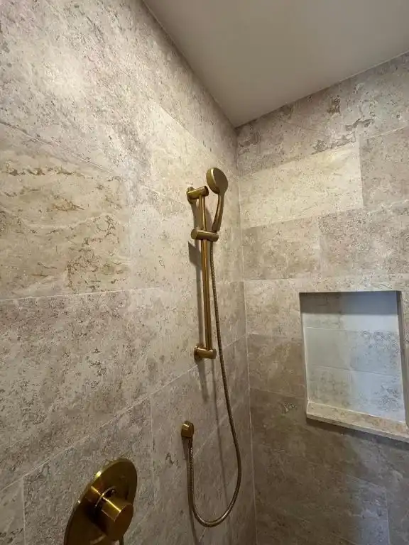 Regadera de latón en un baño de piedra.