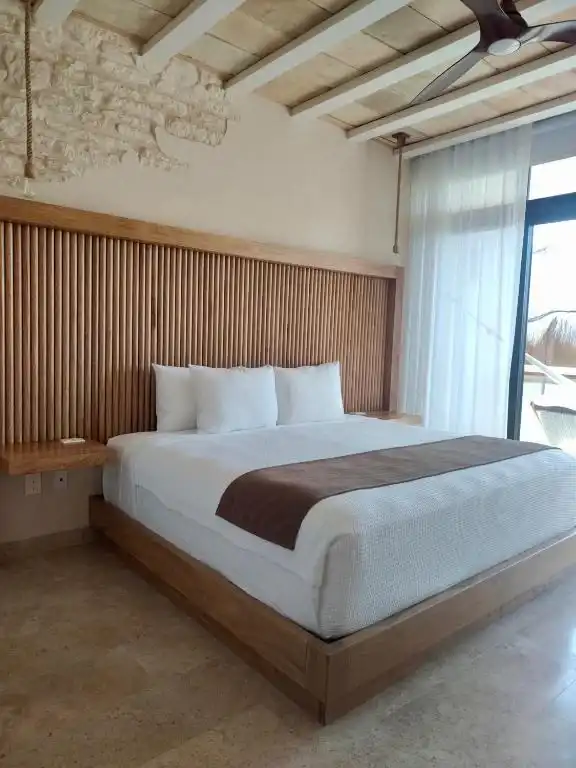 Cama con cabecera de listones de madera, bajo un techo de vigas.
