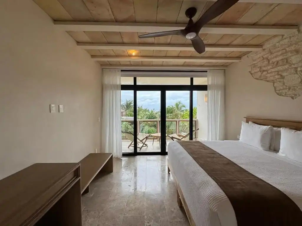 Habitación con cama y ventanal, y una banca de madera a los pies.