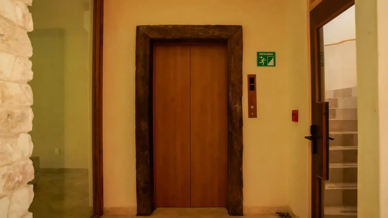 El elevador del hotel, con marco de madera y la señalética de las escaleras.