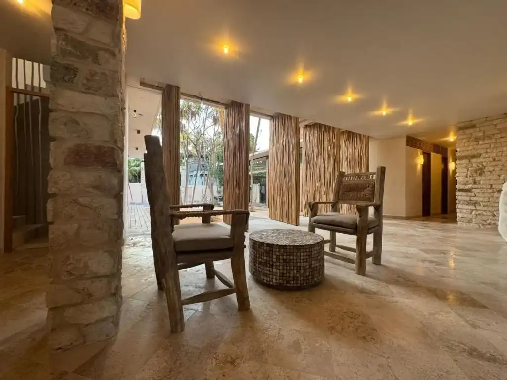 Estar interior con sillones de madera y muro de piedra.