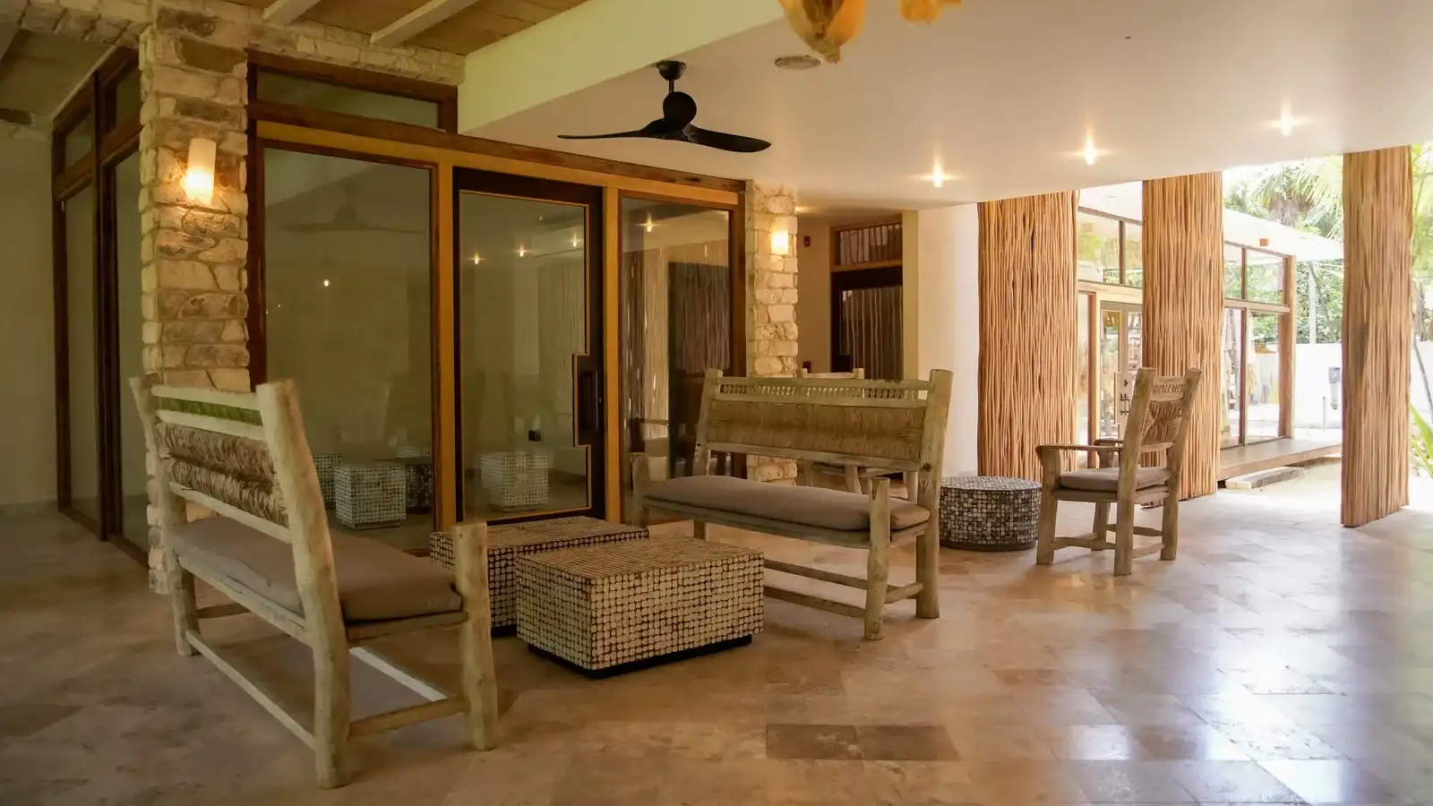 Sala de estar con sillones de madera, ventanales y ventilador de techo.
