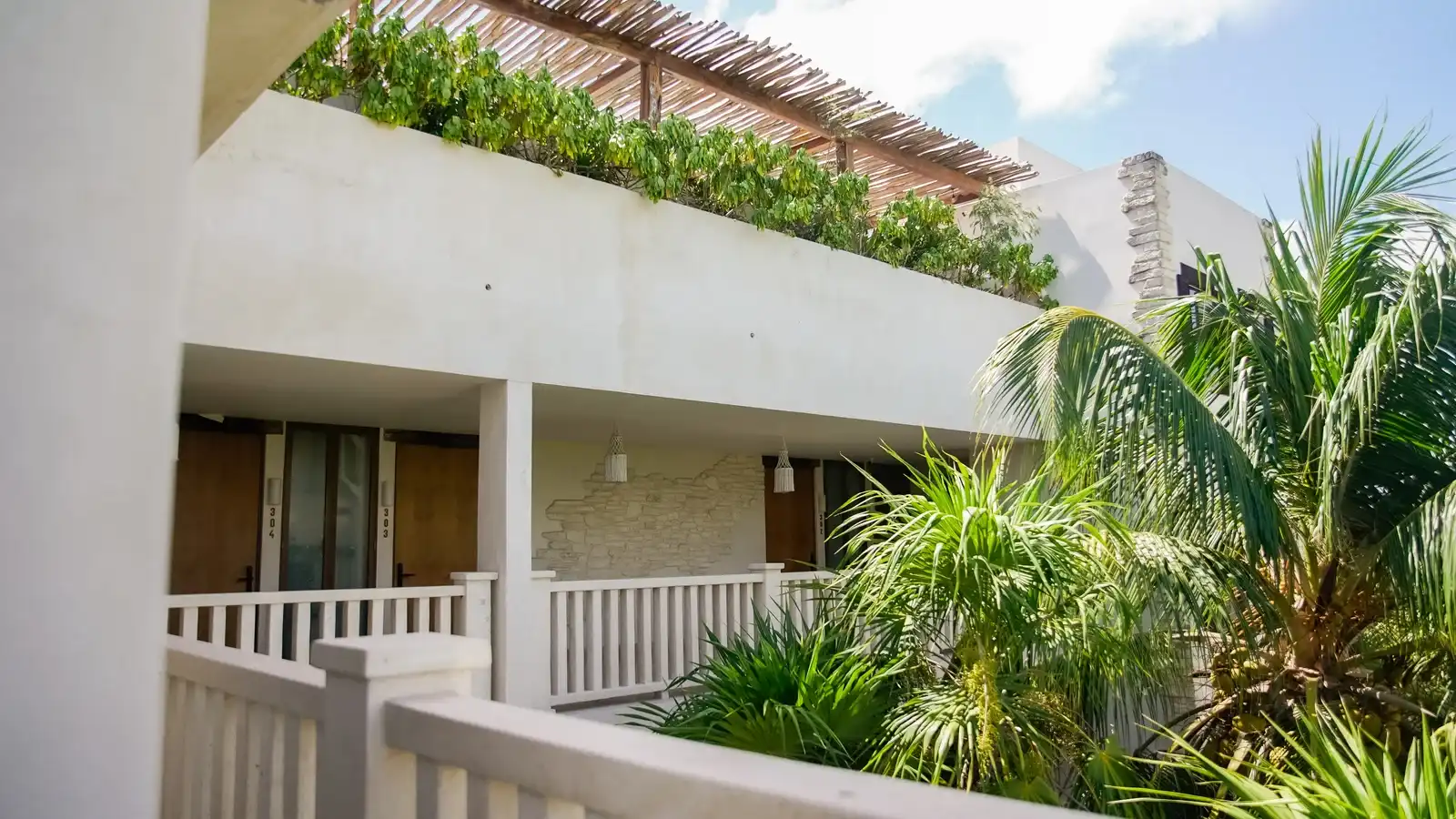 Edificio blanco del hotel con sus balcones, entre la vegetación del jardín.