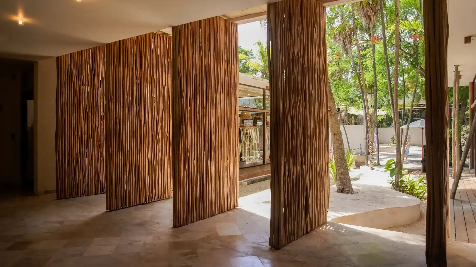 Pasillo con columnas de troncos, abierto al jardín de palmeras.