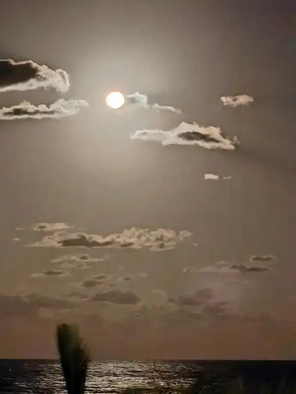 La luna llena sobre el mar, entre nubes.