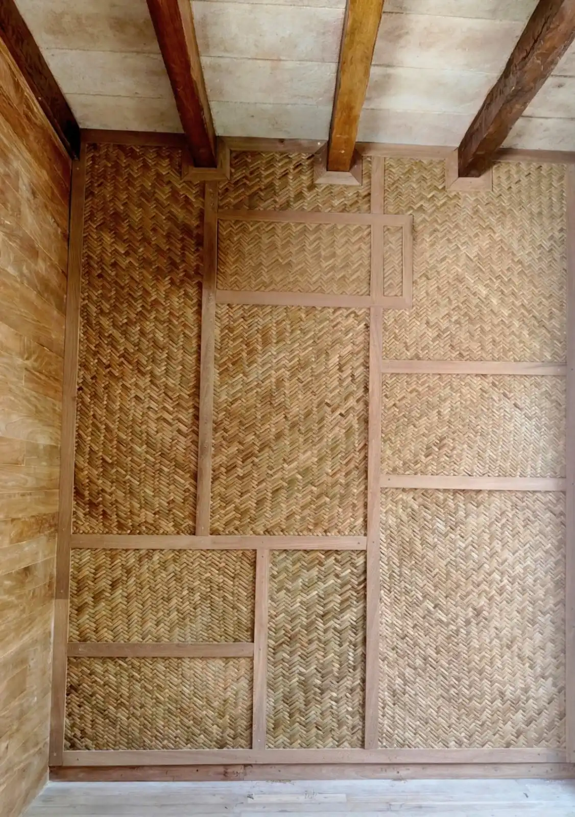 Muro de palma tejida en espiga, entre vigas de madera.