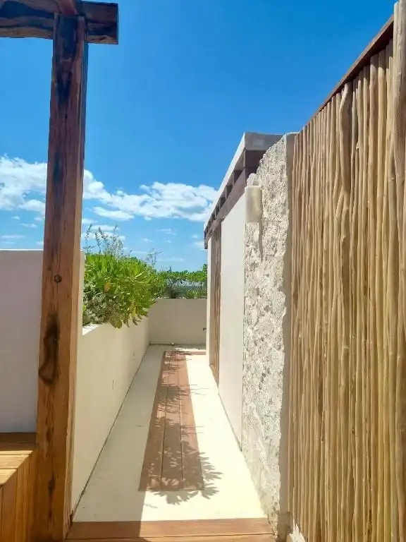 Paso estrecho entre un muro de piedra y una cerca de bambú.