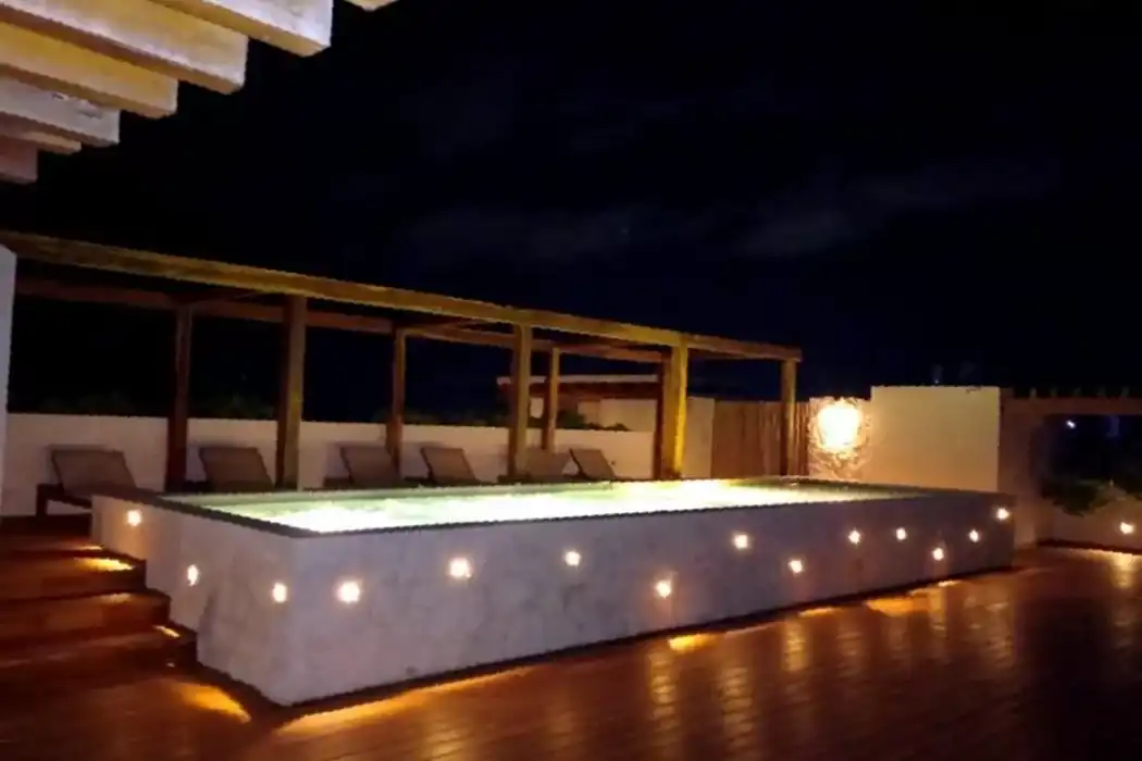 La alberca del roof top de noche, iluminada por dentro y por las luces empotradas en su muro.