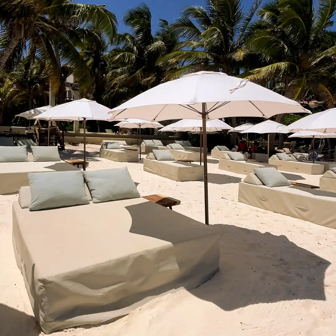 Camastros dobles con cojines bajo sombrillas blancas, en la playa